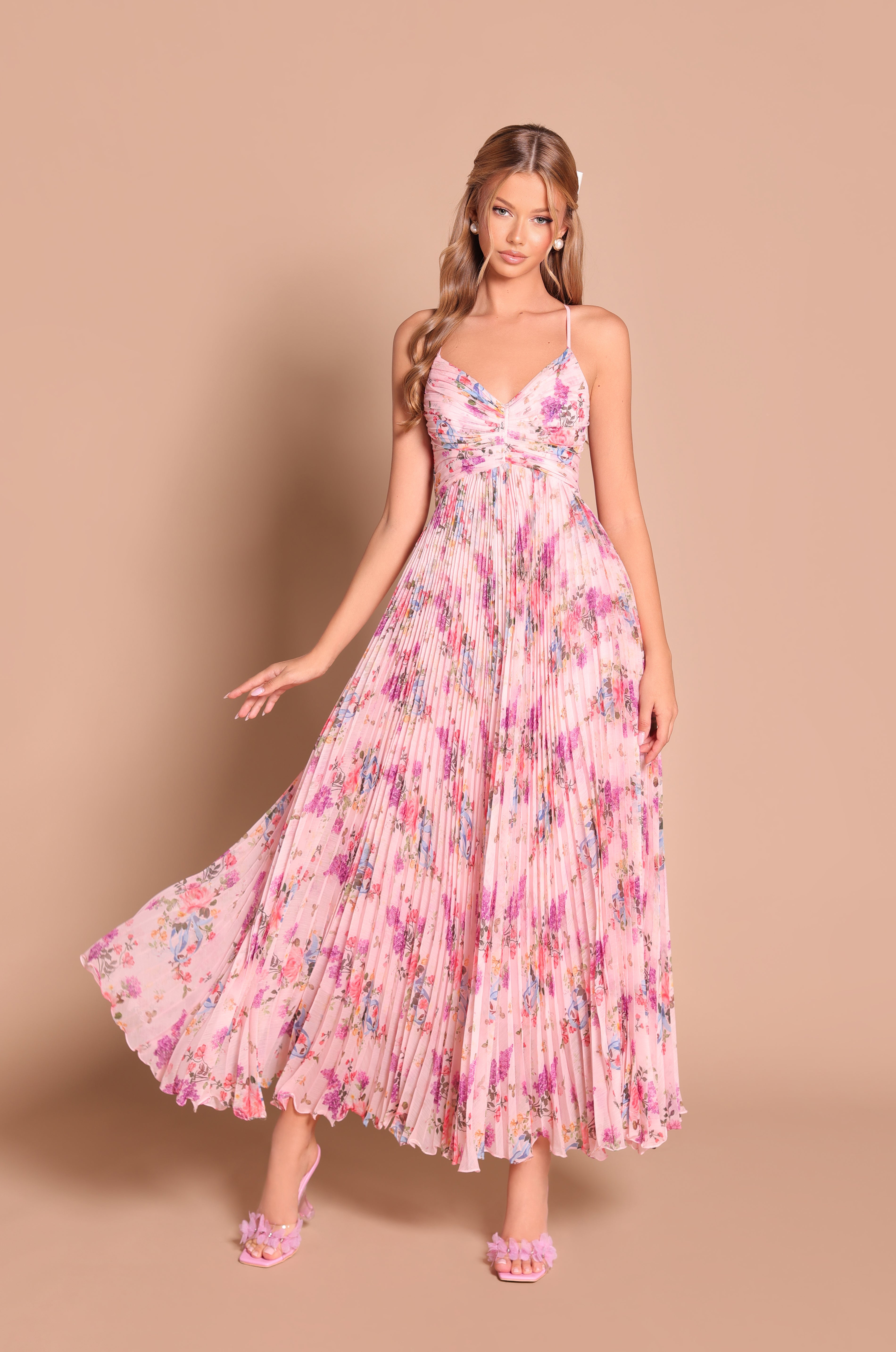 A woman models the Pleated Blush Pink Floral Maxi Dress: Florinne with spaghetti straps and pink heeled sandals, standing against a plain beige background.